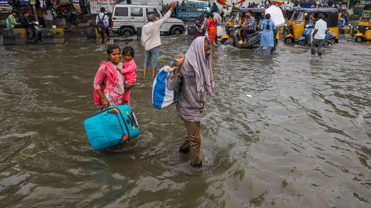 Commuters make their way through a flooded road at a low-lying area near swollen Musi river following heavy rains, in Hyderabad